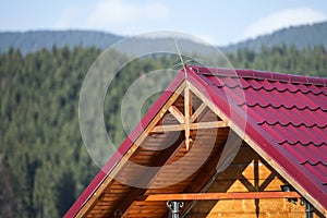 Close-up detail of new modern house top with shingled red roof and wooden sidings on foggy spruce mountains background.