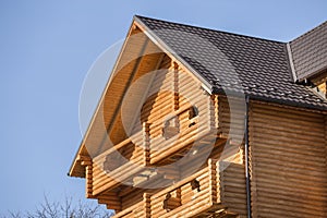 Close-up detail of new modern wooden warm ecological cottage house top with shingled brown roof and wooden sidings on blue sky