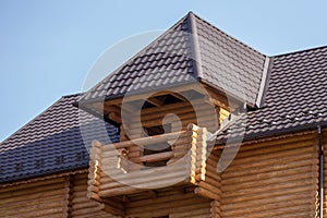 Close-up detail of new modern wooden warm ecological cottage house top with shingled brown roof and wooden sidings on blue sky