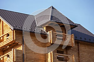 Close-up detail of new modern wooden warm ecological cottage house top with shingled brown roof and wooden sidings on blue sky