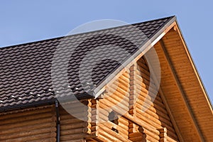 Close-up detail of new modern wooden warm ecological cottage house top with shingled brown roof and wooden sidings on blue sky