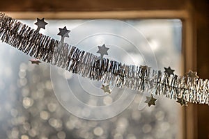 Close-up detail new year Christmas decoration, silver stars and rain on window light blurred bokeh background. Sparkling DIY