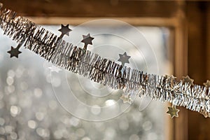 Close-up detail new year Christmas decoration, silver stars and rain on window light blurred bokeh background. Sparkling DIY