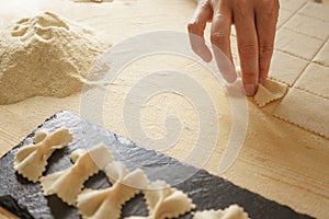 Close up detail of process of homemade vegan farfalle pasta with durum wheat flour. The cook kneads the dough on the wooden