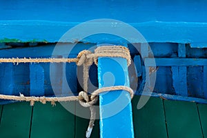 Close up, detail shot and background of an old wooden fishing boat painted blue and green paint. You see a bench to which two