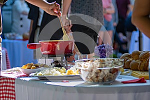 Close up detail shot of person's arm stirring a traditional tasty delicious pot of hot melted liquid swiss cheese fondue