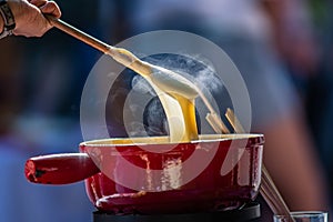 Close up detail shot of person's arm stirring a traditional tasty delicious pot of hot melted liquid swiss cheese fondue
