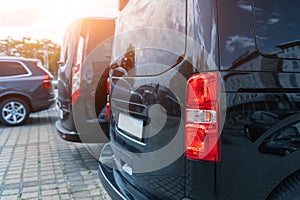 Close-up detail tail light view of many modern luxury black vans parked in row at car sale rental leasing dealer against