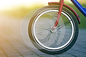 Close-up detail of teenager bicycle front wheel on gray pavement blurred bokeh background on bright sunny day. Urban comfortable