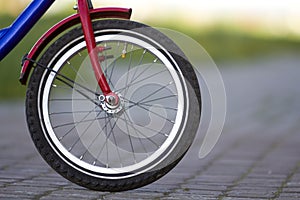 Close-up detail of teenager bicycle front wheel on gray pavement blurred bokeh background on bright sunny day. Urban comfortable t