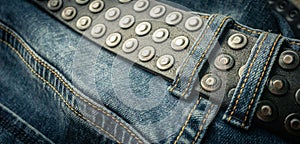 close up detail of an unbuckled leather belt on a faded pair of blue jeans
