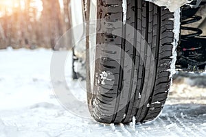 Close-up detail view of car wheel with unsafe summer tread tire during driving through slippery snow road at winter