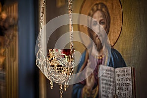 Hanging oil candle in church in front of religious iconography