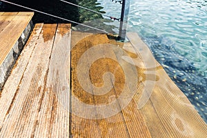 Close-up detail view of natural wooden stair steps of larch ladder into clean blue water of lake, sea or pond. Waterpoof