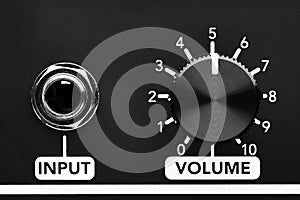 Close up detail of volume control knob and input jack of a black guitar amplifier