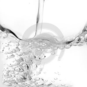 Close-up detail of water pouring on a transparent crystal bowl and white background