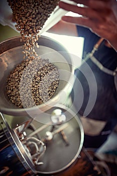 close up detail of whole grain coffee spilling from plastic dish into a preparation machine by caucasian man
