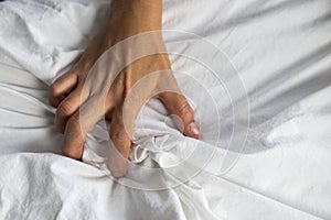 Close up detail of a womens hand grabbing on to the bed sheets, intimacy, erotic concept