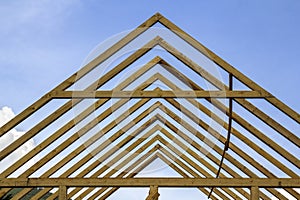 Close-up detail of wooden high steep roof framing under construction. Timber frame of natural materials against bright sky.