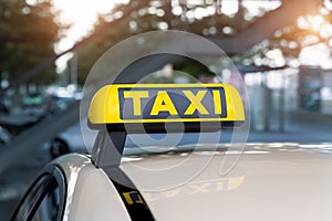 Close-up detail yellow taxi symbol on cars roof stand waiting at parking of airport terminal or railway station against