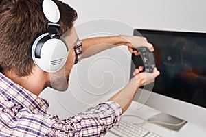 Close up detail of young bearded male gamer playing games on personal computer with controller in headphones, talking