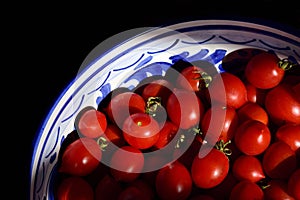 Close up and detailed shot of fresh red small tomatoes lying in an ornate ceramic bowl and photographed from above, against the