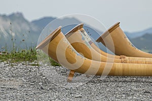 Close-up, detailed view of 3 wooden alphorns lying next to each other with the Austrian Alps in the background.