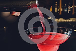 Close up details of barman pouring vodka cosmopolitan cocktail in martini glass.