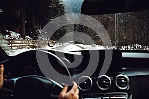 Close up details of driver driving a modern car. Inside of car details, drivers view through windshield. Winter mountain landscape