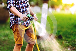 Close up details of gardener using hosepipe watering the lawn, grass and plants