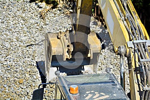 Close up details of an industrial excavator working on a construction site. Excavator bucket levels gravel on the roadway. Men at
