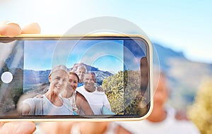 Close up of device screen while active senior people pose together for a selfie outdoors. Group of mature people