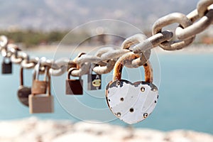 Close up of different old rusty love locks on chain against the sea. Selective focus. Blurred background