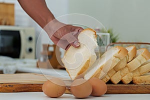 Close-up dining table in kitchen with fresh bread and eggs, An Asian man\'s hand reached in picked up several pieces
