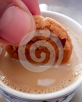 Close up dipping biscuit cookie into tea mug