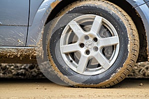 Close up of dirty car wheel with rubber tire covered with yellow mud