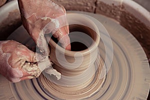 close-up dirty hands of potter man creating with fingers and pressure an earthen jar pot of white clay on the potter`s wheel