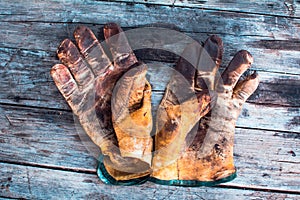 A Close up of a dirty leather work gloves on a wooden table stained with grease and oil