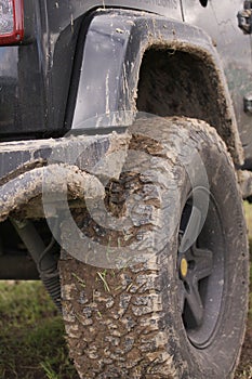 Close up of dirty SUV after driving heavy off-road in wet terrain. Wheels soiled in mud and dirt.