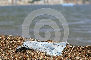 Close-up of a discarded used face mask lies in the surf zone on a sandy pebble beach. Budva, Montenegro