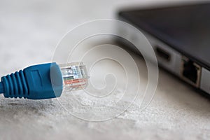 Close-Up of a Disconnected Blue Ethernet Cable Near a Laptop on a White Surface