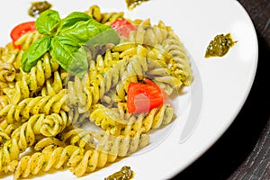 Close-up of dish of pasta with pesto genovese sauce and vegetables, tomato and basil