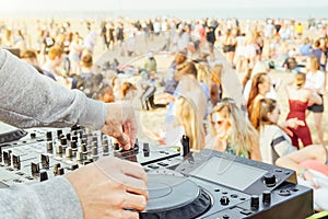 Close up of DJ`s hand playing music at turntable at beach party festival - Crowd people dancing and having fun in club outdoor