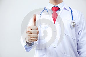 Close up of doctor in coat with stethoscope giving thumbs up in white isolated background