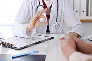 Close up of a doctor hand showing ok sign while phusician and his patient discussing medical records after health