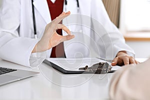 Close up of a doctor hand showing ok sign while phusician and his patient discussing medical records after health