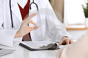 Close up of a doctor hand showing ok sign while phusician and his patient discussing medical records after health