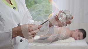 Close-up of doctor heating cup with fire and going to blurred male patient lying on couch at the background