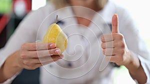 Doctor holding ripe yellow pear in hand and showing thumb up sign