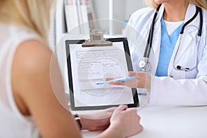 Close up of a doctor and patient hands while phisician pointing into medical history form at clipboard